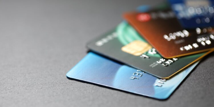 A stack of various credit cards arranged on a dark surface, showing different colors and designs.