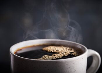 Close-up of a white cup filled with dark coffee and steam rising from the surface.