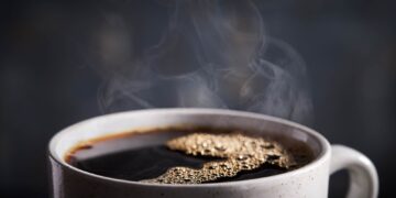 Close-up of a white cup filled with dark coffee and steam rising from the surface.