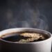Close-up of a white cup filled with dark coffee and steam rising from the surface.