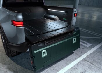 Open tailgate of an electric pickup truck showing the cargo bed and interior lighting.