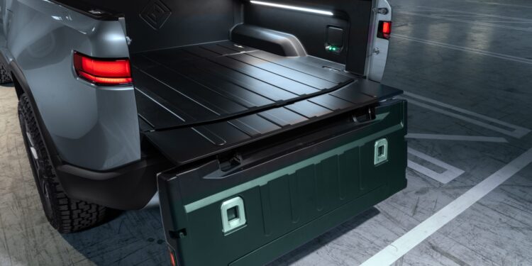 Open tailgate of an electric pickup truck showing the cargo bed and interior lighting.
