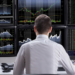 Individual seated at a desk with multiple computer monitors displaying stock market charts and data.
