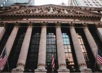 Facade of the New York Stock Exchange featuring columns and flags.
