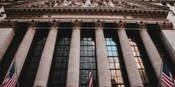 Facade of the New York Stock Exchange featuring columns and flags.