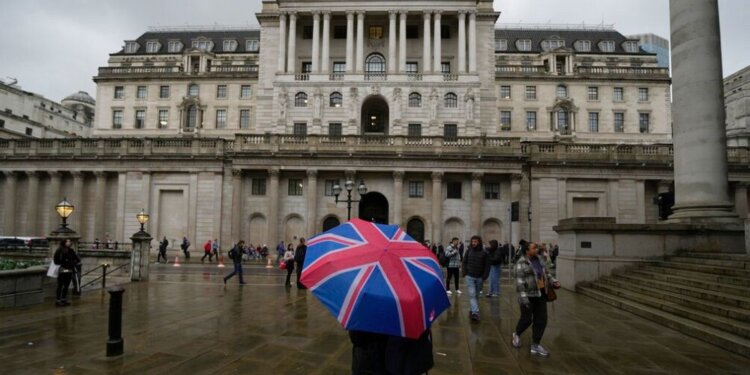 Individual holding a Union Jack umbrella in front of the Bank of England building on a rainy day.