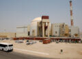 Exterior view of the Iran nuclear power plant with a bus parked nearby and storage containers in the foreground.