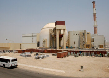 Exterior view of the Iran nuclear power plant with a bus parked nearby and storage containers in the foreground.