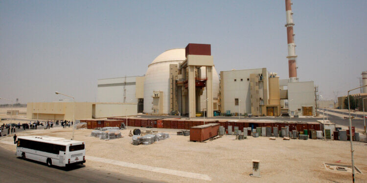 Exterior view of the Iran nuclear power plant with a bus parked nearby and storage containers in the foreground.