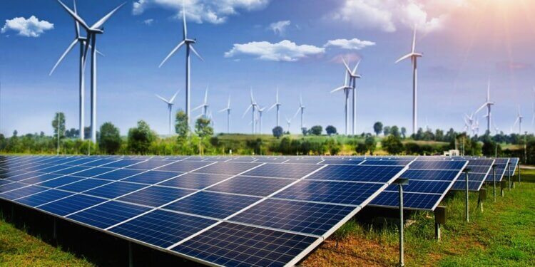 Rows of solar panels in a field with wind turbines in the background under a clear blue sky.