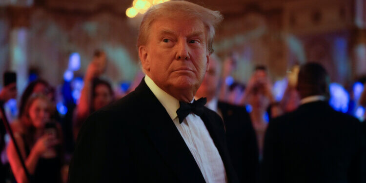 Donald Trump wearing a tuxedo at an event with attendees in the background.