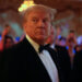 Donald Trump wearing a tuxedo at an event with attendees in the background.
