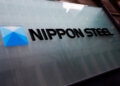 Nippon Steel company logo displayed on a glass surface with a blue geometric design.