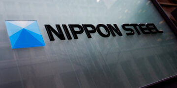 Nippon Steel company logo displayed on a glass surface with a blue geometric design.