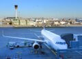 Commercial airplane parked at an airport terminal with ground crew and equipment nearby.