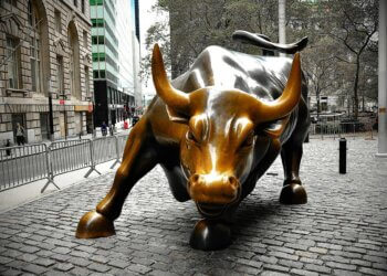 Bronze sculpture of a charging bull located in a city setting with cobblestone pavement.
