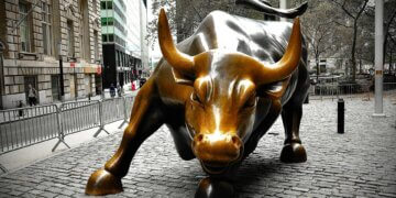 Bronze sculpture of a charging bull located in a city setting with cobblestone pavement.