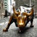 Bronze sculpture of a charging bull located in a city setting with cobblestone pavement.