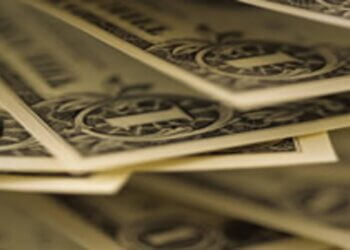 Close-up view of stacked dollar bills with detailed designs and serial numbers visible.