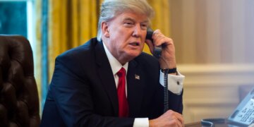 Donald Trump speaking on the phone while seated at a desk in the Oval Office.