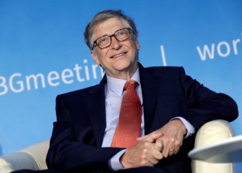 Bill Gates smiling while seated in a chair during a conference event.