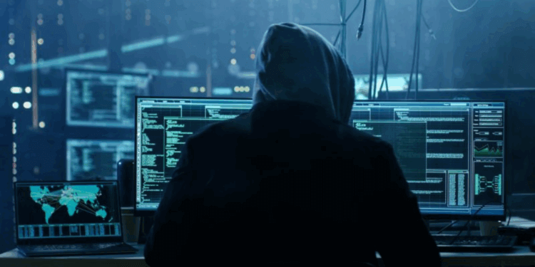 Individual in a hoodie working on multiple computer screens displaying code and data analysis.