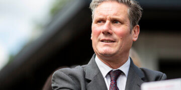 Man wearing a suit with a tie, looking slightly to the side with a neutral expression.