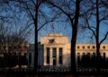 Federal Reserve building viewed through bare trees during sunset with clear sky.