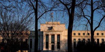 Federal Reserve building viewed through bare trees during sunset with clear sky.