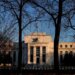 Federal Reserve building viewed through bare trees during sunset with clear sky.