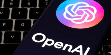OpenAI logo displayed on a smartphone screen with a keyboard in the background.