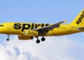 Yellow Spirit Airlines aircraft flying in the sky with clouds in the background.