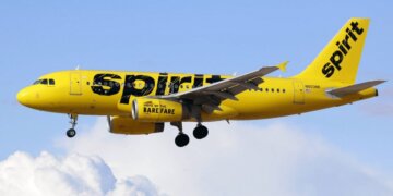Yellow Spirit Airlines aircraft flying in the sky with clouds in the background.