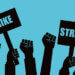 Illustration of multiple raised fists holding signs that say 'Strike' against a blue background.