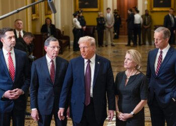 Donald Trump speaking with Senate GOP members in a formal setting with security personnel in the background.
