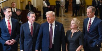 Donald Trump speaking with Senate GOP members in a formal setting with security personnel in the background.