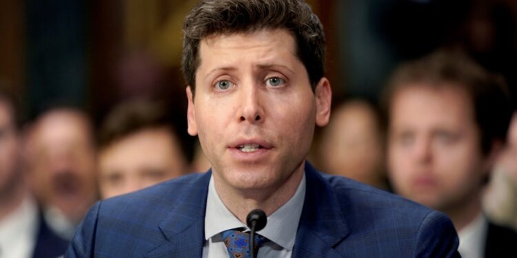 Man in a blue suit speaking into a microphone during a formal hearing setting.