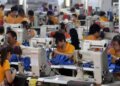 Group of workers in orange shirts using sewing machines in a factory setting.