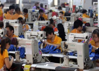 Group of workers in orange shirts using sewing machines in a factory setting.
