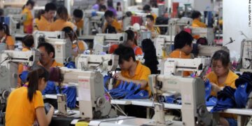 Group of workers in orange shirts using sewing machines in a factory setting.