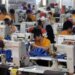 Group of workers in orange shirts using sewing machines in a factory setting.