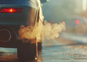 Close-up of a car tailpipe emitting thick exhaust gases in an urban setting.