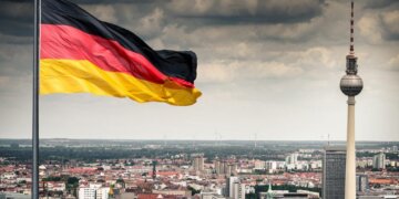 German flag waving in the foreground with the Berlin TV Tower visible in the background.