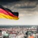 German flag waving in the foreground with the Berlin TV Tower visible in the background.