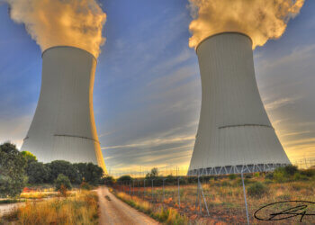 Two cooling towers of a nuclear power plant emitting steam against a sunset sky.