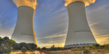 Two cooling towers of a nuclear power plant emitting steam against a sunset sky.