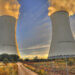 Two cooling towers of a nuclear power plant emitting steam against a sunset sky.