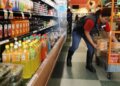 Grocery store employee placing containers of fruit on a cart in the beverage aisle.