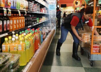 Grocery store employee placing containers of fruit on a cart in the beverage aisle.