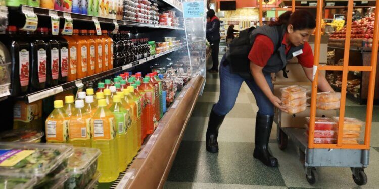 Grocery store employee placing containers of fruit on a cart in the beverage aisle.